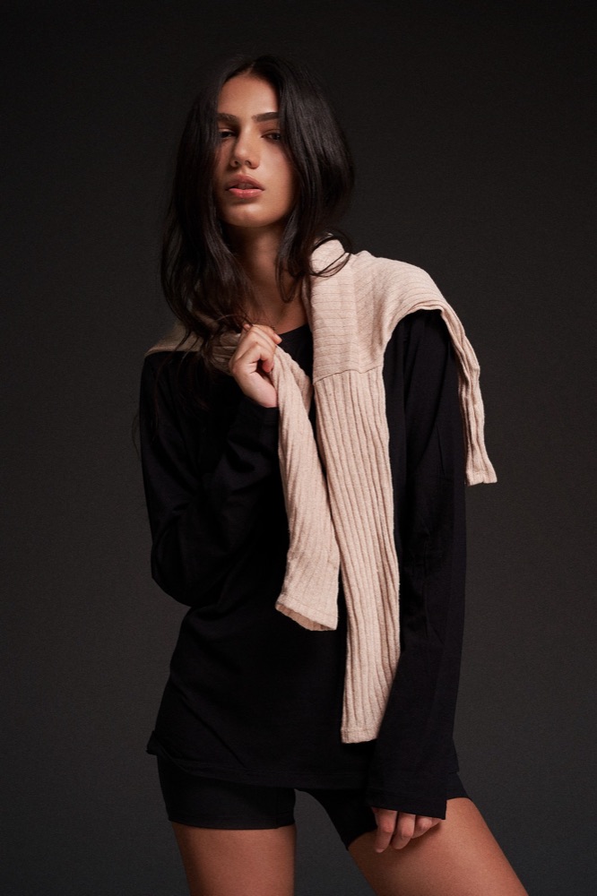 Woman in black activewear with a cream sweater over her shoulders
